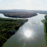 Imagem aérea do encontro das águas dos rios das Velhas e São Francisco, na Barra do Guaicuí (MG), com reflexo do sol no rio das Velhas