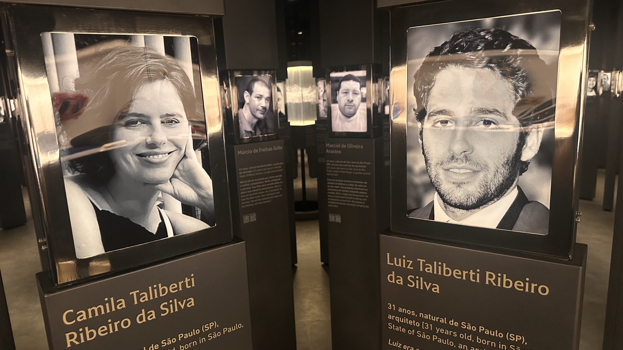 Painéis iluminados com fotos em preto e branco de Camila e Luiz Taliberti no Memorial Brumadinho, ao lado de outras vítimas da Vale, ilustrando o artigo sobre o livro de Helena Taliberti.