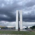 Fotografia do Congresso Nacional sob céu de tempestade, inserida para ilustrar visualmente o clima de tensão e a urgência da pauta ambiental que aguarda os novos parlamentares.